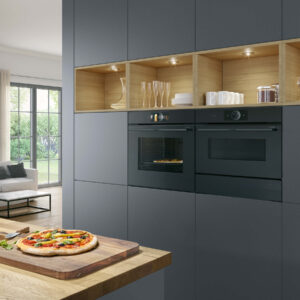 Moderne Bosch Einbauküche mit dunklen Fronten, integrierten Backöfen und beleuchteten Holzregalen, Pizza auf Holzbrett im Vordergrund bei A2 Küchen