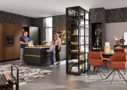 Moderne Küche in Schwarz und Holz mit Kochinsel und Glasvitrine, integrierte Beleuchtung und Geräte, Familie kocht gemeinsam in wohnlicher Atmosphäre