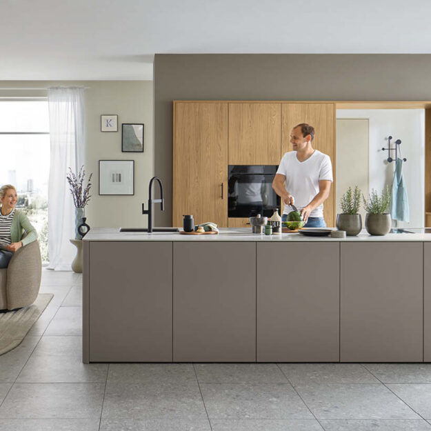 Moderne, grifflose Küche mit Kochinsel in matten Grautönen und Holzrückwand, integrierte Geräte und großzügige Arbeitsfläche für entspanntes Kochen im offenen Wohnraum