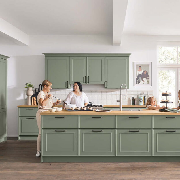 Gemütliche Landhausküche in sanftem Salbeigrün mit großer Arbeitsfläche und warmen Holzelementen, perfekt für Familien und gemeinsames Kochen im Alltag